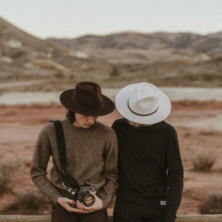 Two people walking through the landscape wearing Will & Bear fedoras, including the Cooper Bone White Upturned Fedora.