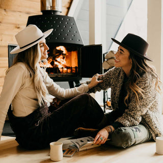 Couple chatting beside a fireplace wearing Will & Bear fedoras, including the Cooper Bone White Upturned Fedora.
