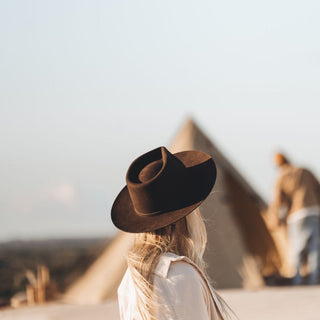 Woman wearing the Will & Bear Cooper Coffee Brown Western Hat at a desert campsite with triangular tents in the background.