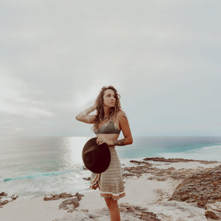 Woman walking on coastal cliffs wearing the Will & Bear Cooper Coffee Brown Western Hat with a round crossbody bag.