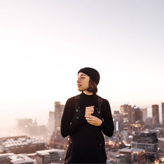 Woman standing on rooftop with Will & Bear Doc Black Wool Fisherman’s Beanie, looking out over the city skyline at sunrise.