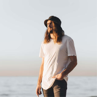 Man walking along the shoreline wearing the Will & Bear Earth Bucket Organic Hemp Bucket Hat in natural sunlight.