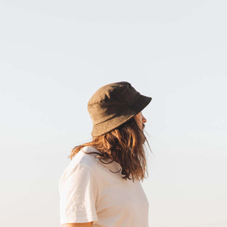 Man wearing the Will & Bear Earth Bucket Organic Hemp Bucket Hat, looking out over a coastal sunrise.
