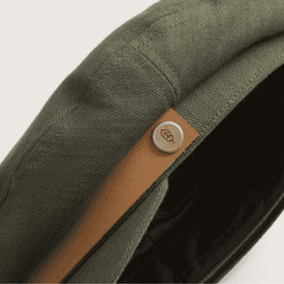 Close-up of Will & Bear Foster Green Fiddler Cap showing the tan hat band and logo-engraved button detail.