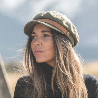 Woman wearing the Will & Bear Foster Green Fiddler Cap standing in a natural landscape with neutral outfit styling.