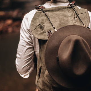 Will & Bear Hat Carry Clips in use, securing a felt hat to a canvas backpack on an outdoor adventure.