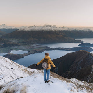 Traveller standing at a snowy summit with Will & Bear Hat Carry Clips securing their hat to their pack.