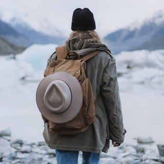 Woman hiking through a snowy landscape with a hat secured to his pack using Will & Bear Hat Carry Clips.