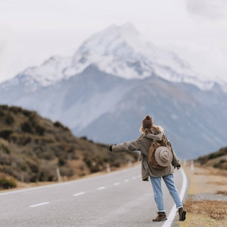 Woman walking along a mountain road with a backpack and Will & Bear Hat Carry Clips securing her hat.