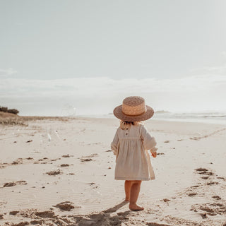 Child in Will & Bear Little Harvey Amber Kids Straw Hat – Standing on the Beach Looking at the Sea.