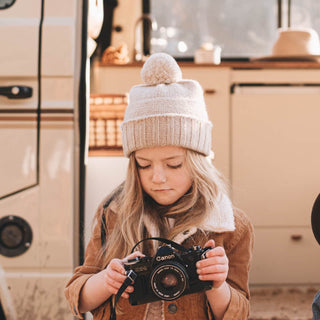 Young Girl Wearing Will & Bear Little Tasman Fawn Kids Wool Cream Beanie Holding a Vintage Camera – Cosy Beanie for Winter Days.