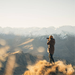 Explorer on a mountain ridge at sunrise wearing the Will & Bear Levi Mustard Wool Beanie, surrounded by clouds and peaks.