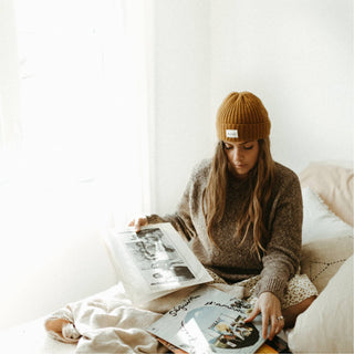 Woman indoors reading with the Will & Bear Levi Mustard Wool Beanie on, styled for cosy homewear.