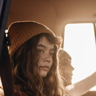 Woman in van wearing the Will & Bear Levi Mustard Wool Beanie, natural light streaming in through window.