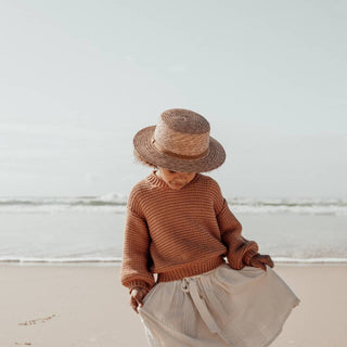 Young Girl Wearing Will & Bear Little Harvey Amber Kids Straw Hat – Natural Wide-Brim Hat for Children on the Beach in Earthy Tones.